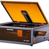 Creality Falcon A1 Pro laser engraver with lid open and camera visible, beside a smartphone showing the monitoring app