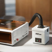 Creality Falcon smoke purifier with a black flexible hose connected, placed beside a white enclosed laser engraver on a desk